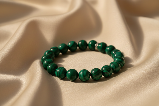 Create a luxurious product photo of a natural malachite crystal bracelet placed on a cream satin fabric with soft folds. Use warm, soft light from one side to create gentle highlights on the beads and enhance the green patterns. Add subtle depth of field to blur the background slightly. No additional objects. High-end jewelry photography feel.